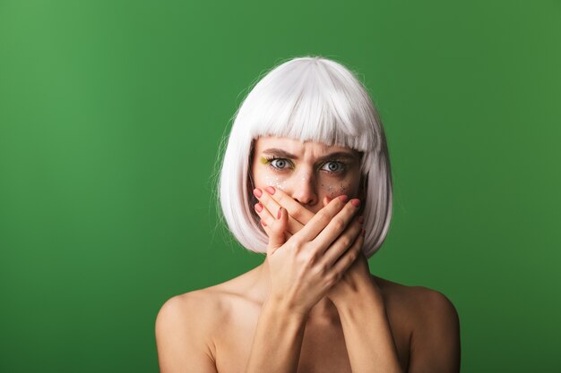 Attractive upset young topless woman wearing short white hair standing isolated, covers her mouth