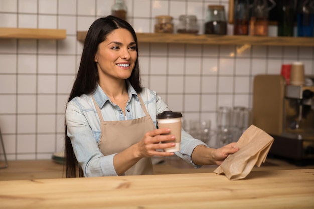 Attractive waitress holding coffee to go and take away food in cafe