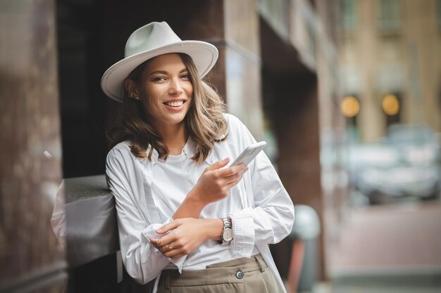 Attractive white Caucasian girl in stylish white clothing and white hat with a mobile phone