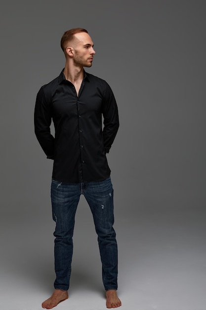 ジーンズと黒のシャツを着た魅力的な白人男性が灰色の背景に完全に成長しているコピースペース