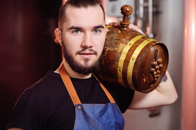 Attractive winemaker holds a wooden barrel of wine