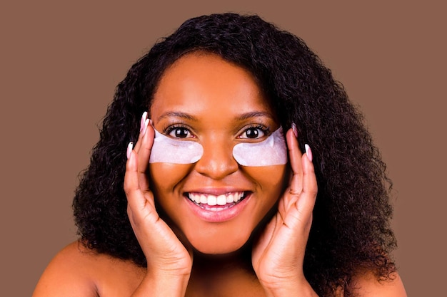 attractive woman applying antifatigue undereye mask in studio brown background