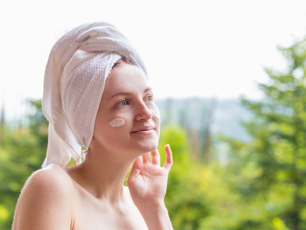 Attractive woman applying moisturizer cream on her face.