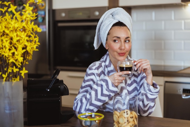 Привлекательная женщина в халате наслаждается утренним кофе и отдыхает на кухне дома.