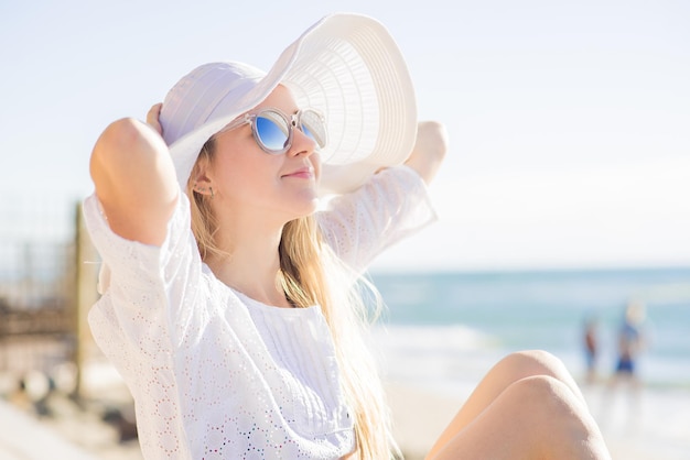 Attractive woman in big hat relaxing on the shore of the ocean or sea