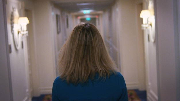 Attractive woman in blue dress searching room in corridor apartment hotel
