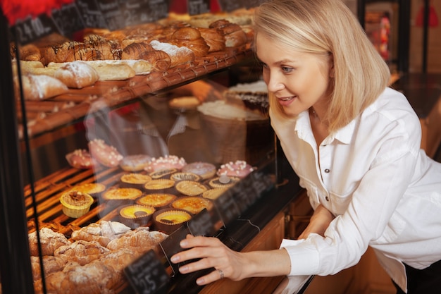 Donna attraente che sceglie deliziosi dessert dalla vetrina al negozio di panetteria