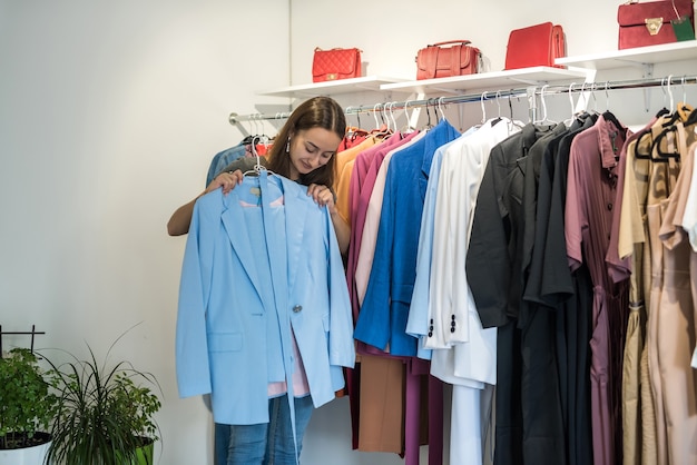 Attractive woman choosing stylish jacket or dress in clothing store