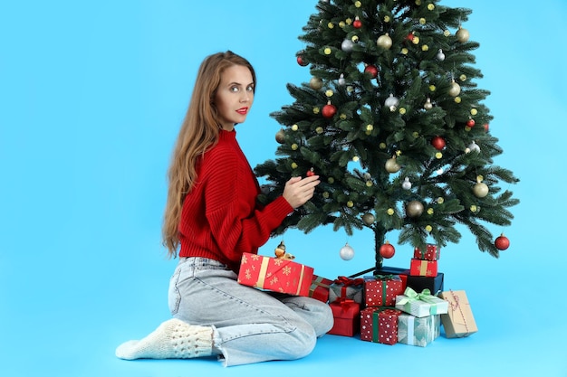 Attractive woman, Christmas tree and gift boxes on blue background