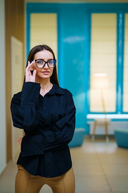 Photo attractive woman in dark shirt and glasses standing arms crossed in hall and smiling female appearance concept full length view