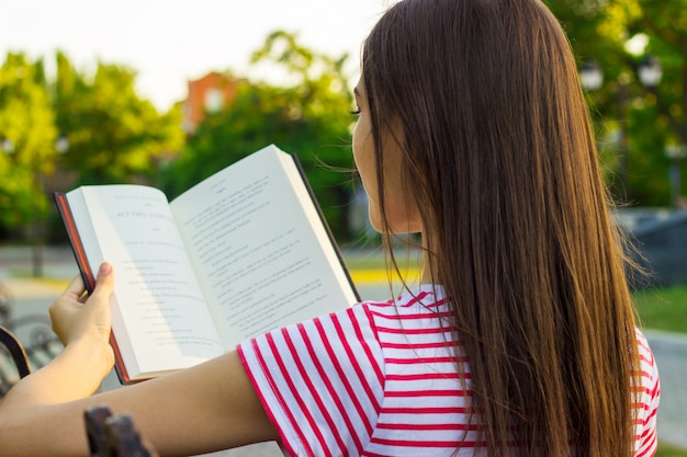 Attractive woman enjoying a book on the bench in the park in summer day. 