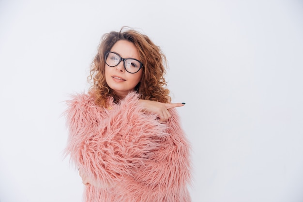 Attractive woman in glasses and pink fur coat. Isolated gray background