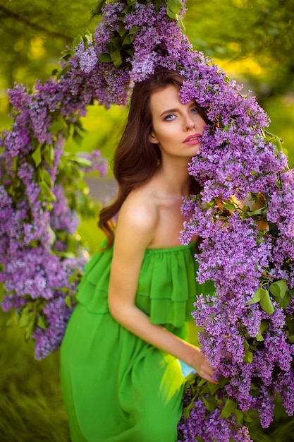 attractive woman in green dress posing near lilac flower decor.