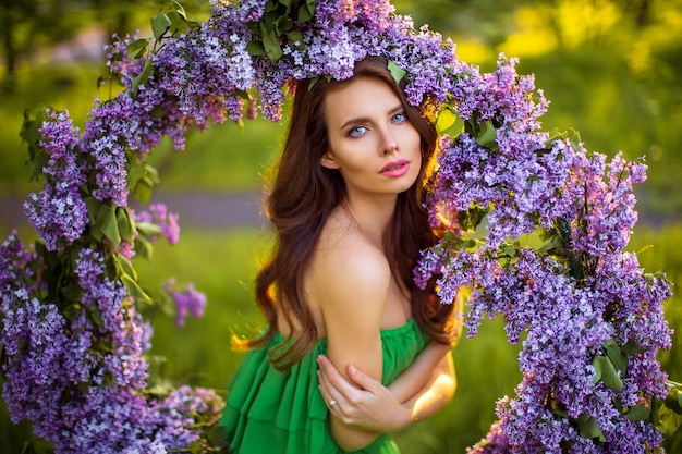 attractive woman in green dress posing near lilac flower decor.