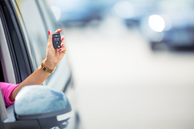 魅力的な女性は車のキーを保持しているウィンドウカーを配ります。