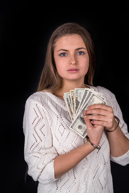 Attractive woman in handcuffs with bribe isolated on black