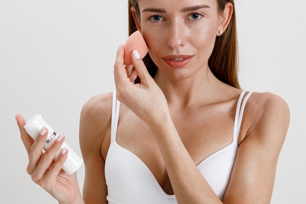 Attractive woman hold pink sponge for applying beauty cosmetic products on face on studio background