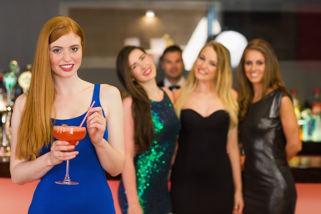 Привлекательная женщина, держащая коктейль, стоя перед ее друзьями