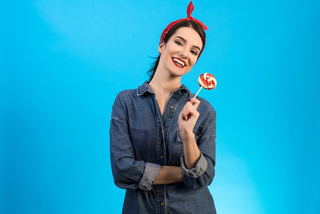 The attractive woman holding a lollipop on the blue background