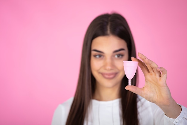 Attractive woman holding menstrual cup standing against pink