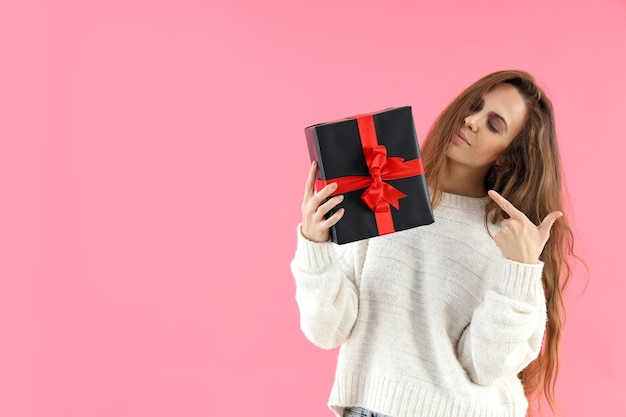 Attractive woman holds gift box on pink background