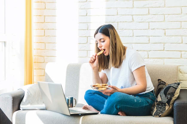 Attractive woman at home on sofa watching tv show and eating waffles