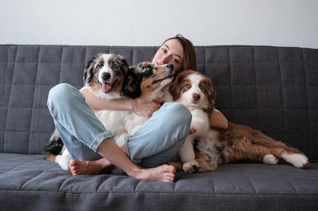 魅力的な女性は3つのメルル色のオーストラリアの羊飼いの子犬の犬を抱きしめます