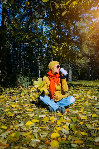 사진 가을 공원에서 매력적인 여자 햇빛에 노란 단풍에 앉아 예쁜 여자 단풍나무 잎을 들고 커피를 마시는 행복한 건강한 라이프 스타일