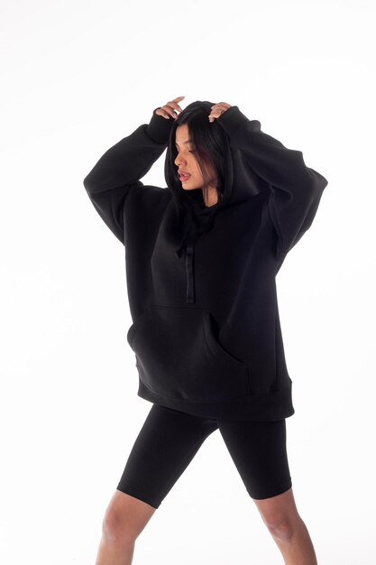 Attractive woman of Latin appearance wears a dark hoodie on a white isolated background The girl looks sexy and happy The elegant brunette is wearing a black sweatshirt Allseason clothing