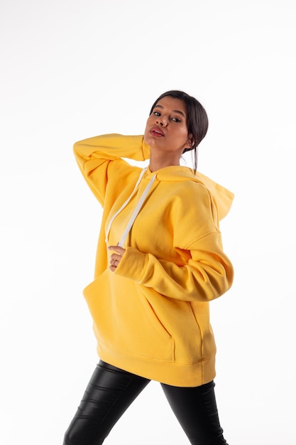 Attractive woman of Latin appearance wears a yellow hoodie on a white background The girl looks sexy and happy The elegant brunette is wearing a bright sweatshirt Allseason clothing