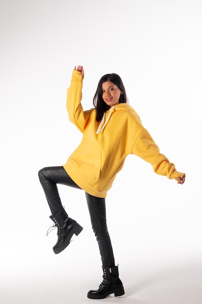 Attractive woman of Latin appearance wears a yellow hoodie on a white background The girl looks sexy and happy The elegant brunette is wearing a bright sweatshirt Allseason clothing