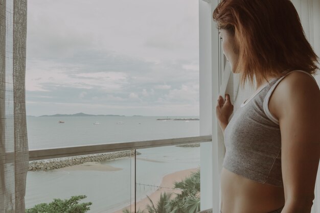 Attractive woman look at the view behind the curtain in the hotel