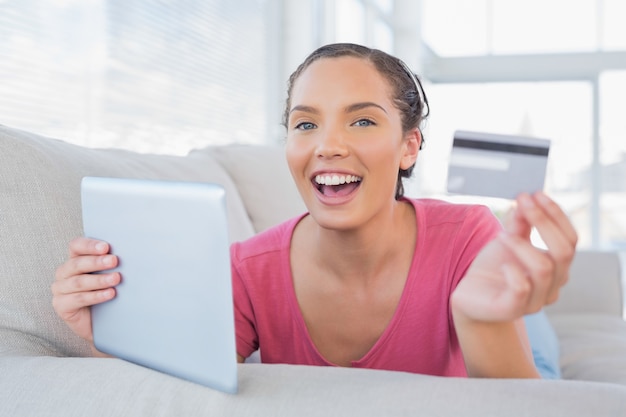 Attractive woman lying on a sofa holding a card and tablet 