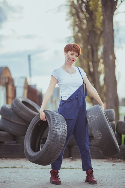 Photo attractive woman mechanic in overalls holding tires