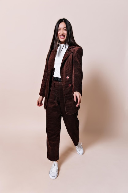 Attractive woman in oversized suit laughs on beige background