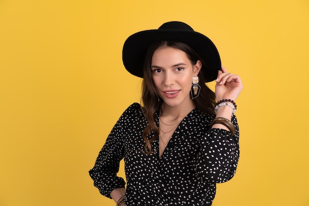 Attractive woman posing isolated on yellow background wearing black hat and dress