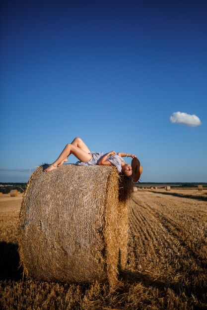Attractive woman posing in the mown wheat fields with sheaf and sky in the village. Hay bales in the field after harvest