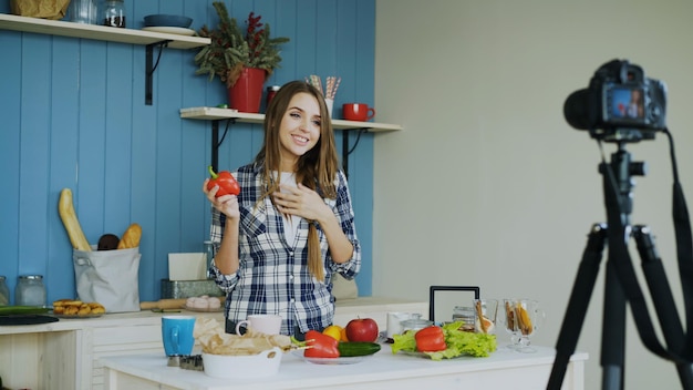 Foto donna attraente che registra video blog sul cibo sano vegetariano sulla fotocamera dslr in cucina