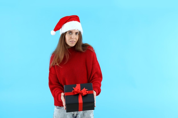 Attractive woman in santa hat holds gift box on blue background