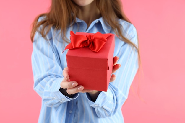 Una donna attraente con un cappello da babbo natale tiene una confezione regalo su sfondo rosa