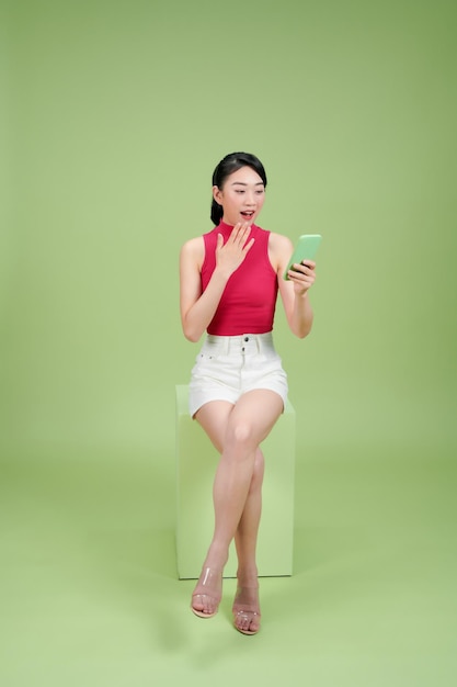 Photo attractive woman sit box browsing her phone isolated on green background