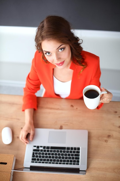 Привлекательная женщина сидит за столом в офисе и работает с ноутбуком