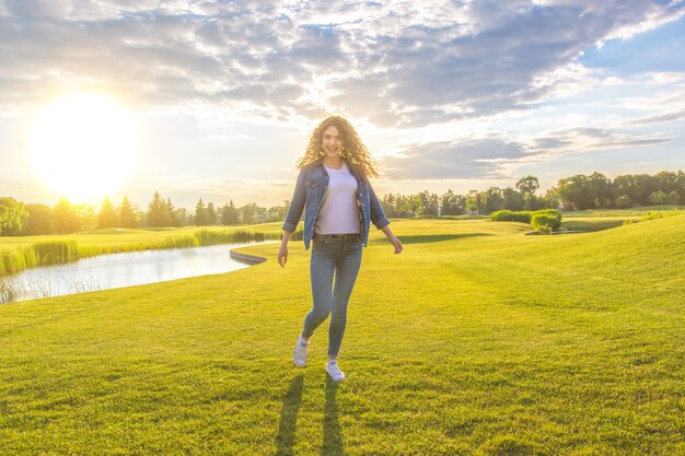 The attractive woman stand on the grass on the sunshine background