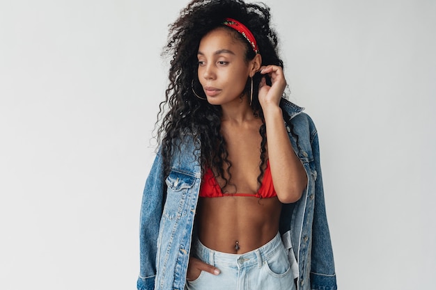 Attractive woman in stylish hipster outfit denim jacket and jeans on white isolated wall