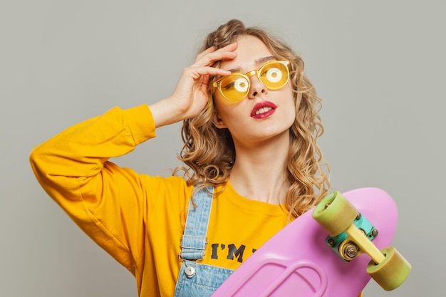 Attractive woman in sunglasses holding skateboard on white background