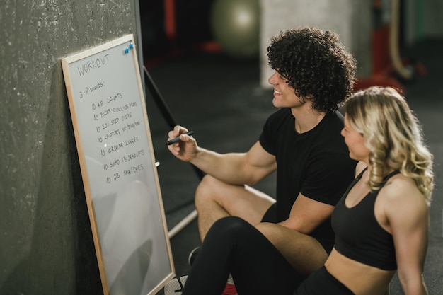 Foto una donna attraente che parla del piano di esercizi con il suo personal trainer in palestra.