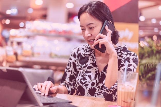 Donna attraente che parla al telefono cellulare mentre lavora al computer portatile seduto in una caffetteria