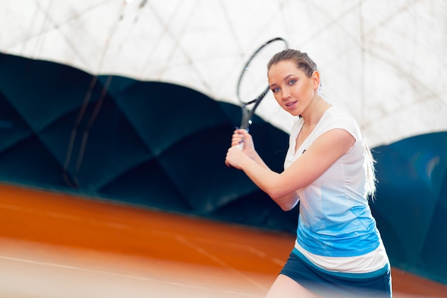 Attractive woman tennis player waiting for service at indoor court