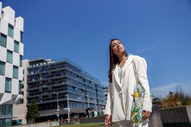 Donna attraente in abito alla moda in piedi sullo sfondo del paesaggio urbano di grattacieli e distogliendo lo sguardo