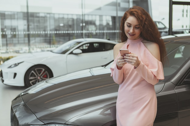 Attractive woman using smart phone at car dealership